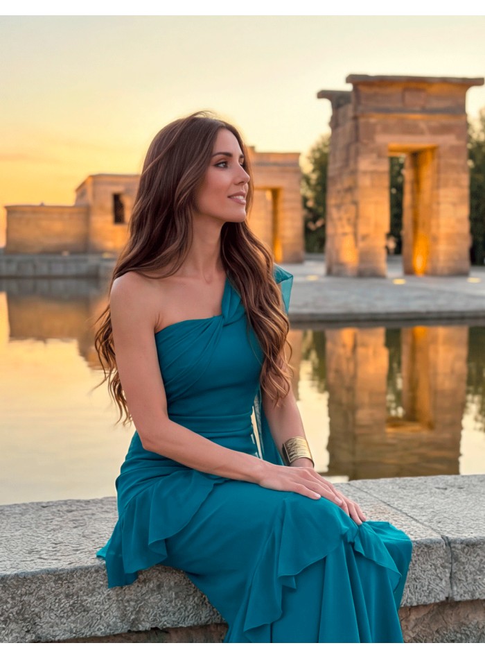 Vestido largo en azul océano con escote asimétrico, capa y volantes. Un diseño elegante, favorecedor y fabricado en España.